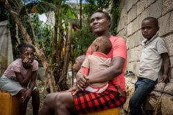 A women sits with a child in her arms, flanked by two other children.