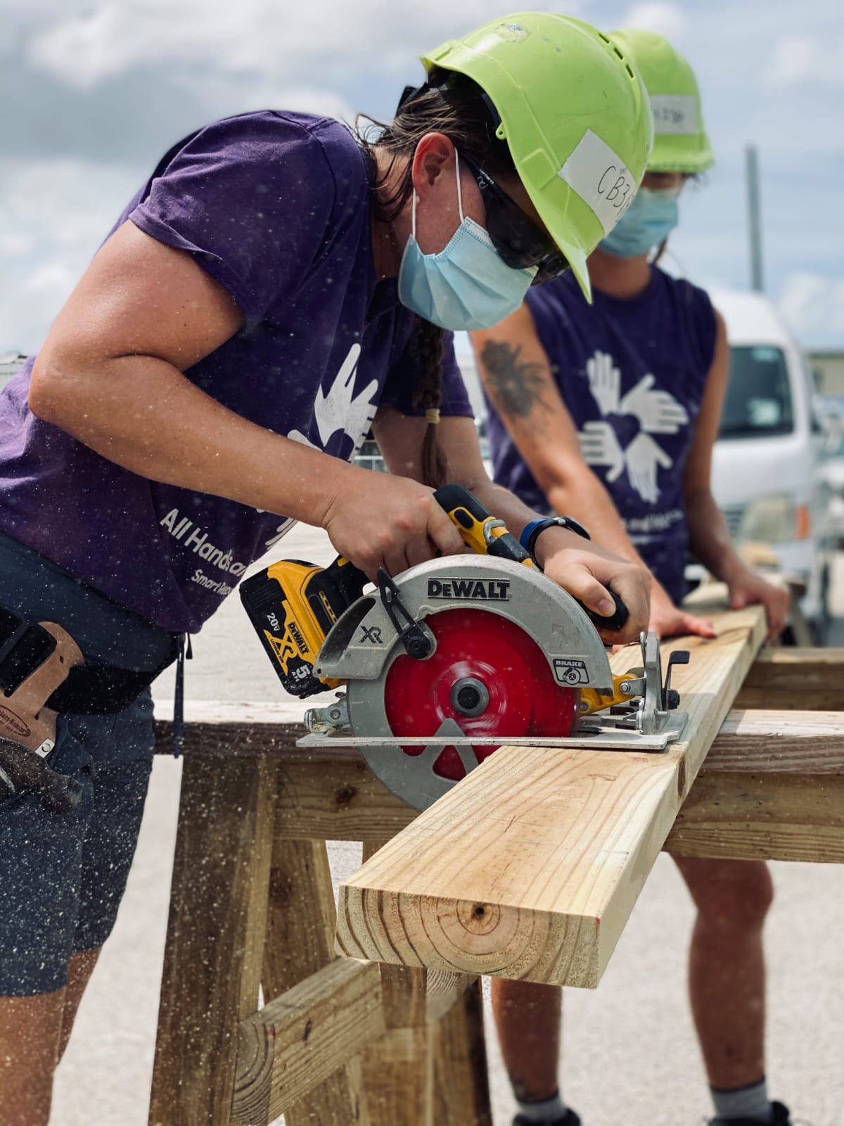 A volunteer with All Hands and Hearts using a saw to cut a plank of wood.