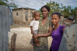 Minouche and her two children standing near their home, a cuboid of steel girders. Malteser International Americas