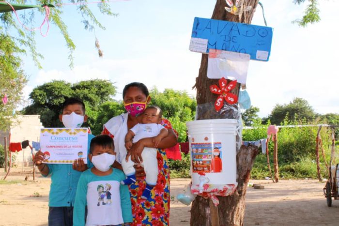 An indigenous woman and her three children stand next to a hand washing station in La Guajira, Colombia.